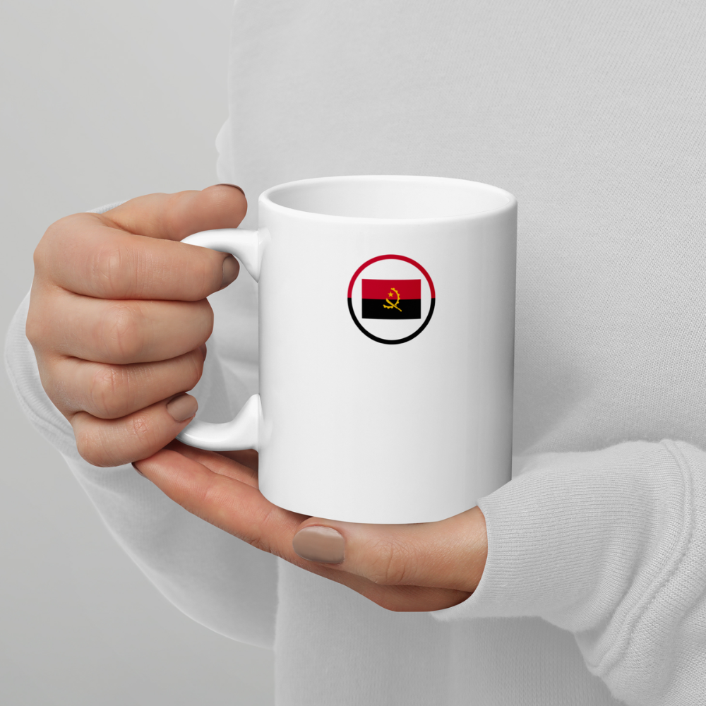 Mug blanc tenu en mains avec emblème du drapeau de l’Angola Personne tenant un mug en céramique blanche avec un emblème circulaire du drapeau de l’Angola imprimé sur la face avant.