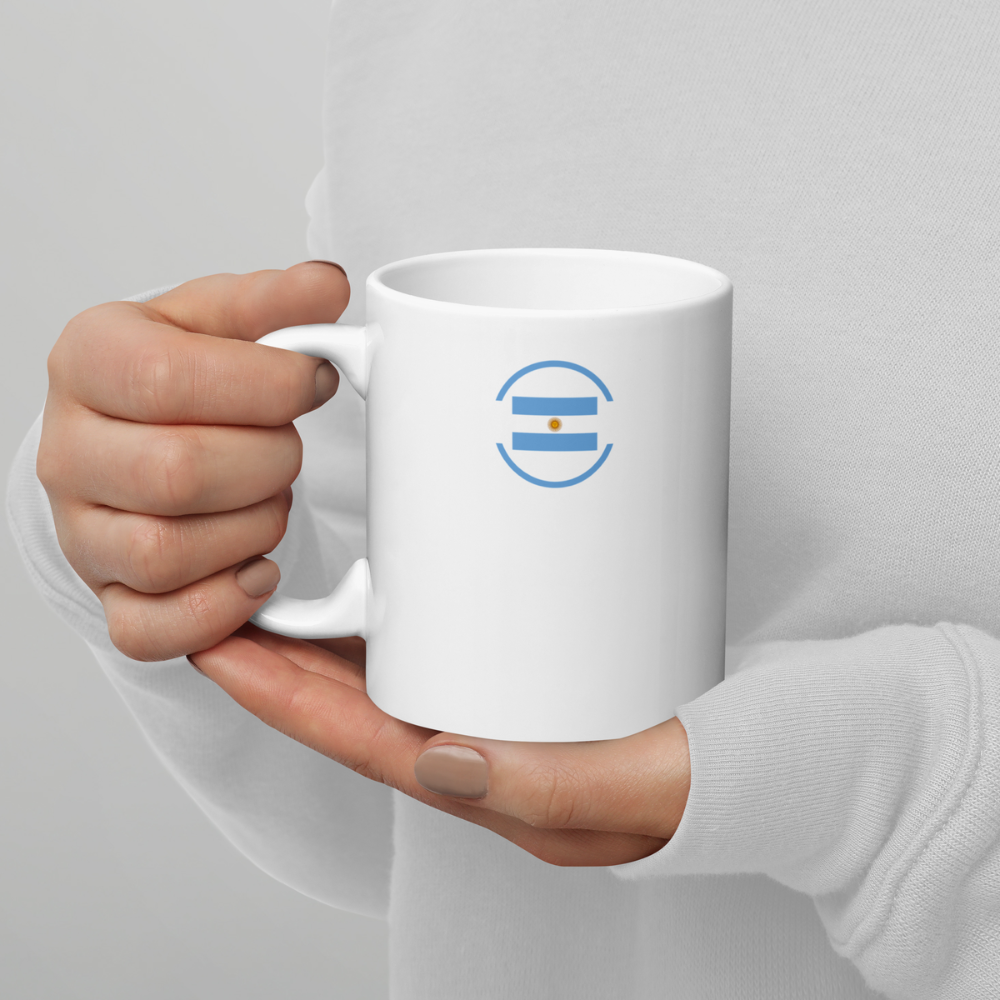 Mug blanc avec drapeau argentin stylisé tenu en mains Mug en céramique blanc vu de face, tenu à deux mains, avec un motif circulaire bleu clair contenant le drapeau argentin.