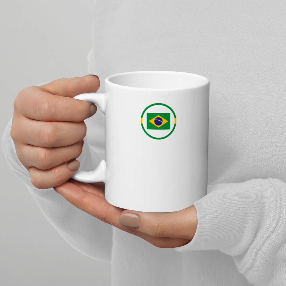 Mug blanc avec drapeau brésilien stylisé tenu en mains Mug en céramique blanc vu de face, tenu à deux mains, avec un motif circulaire vert contenant le drapeau du Brésil.