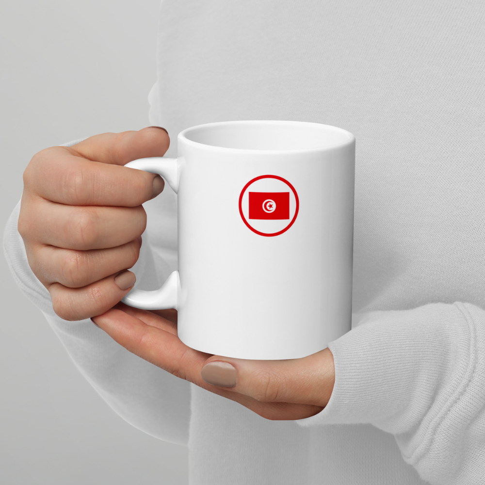 Mug blanc tenu à deux mains avec drapeau tunisien stylisé Personne tenant un mug en céramique blanche avec un drapeau tunisien stylisé en rouge et blanc imprimé au centre.